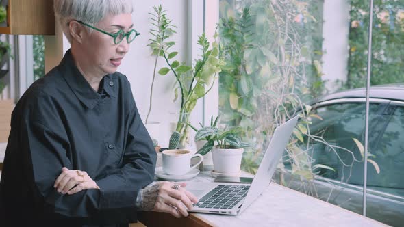 Asian senior woman working on laptop computer on desk in the coffee shop.