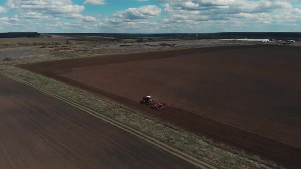 The Tractor Plows the Ground on the Field at the Beginning of the Planting Season. Aerial View 