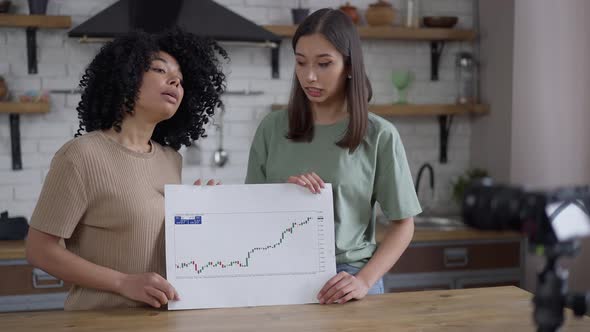 Professional Young Women Pointing at Business Graph Talking at Video Camera Standing in Kitchen