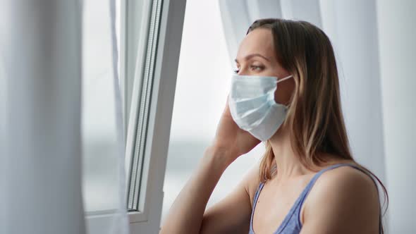 Sickness Woman in Medical Mask and Headache Looking at Window