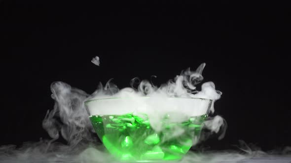 Green Liquid Boils Giving Off Smoke in a Glass Bowl on a Black Background alt