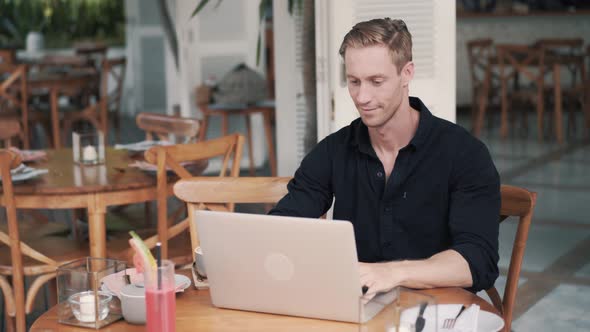 Man Freelancer Sitting at Table and Opening Laptop for Work in Modern Cafe