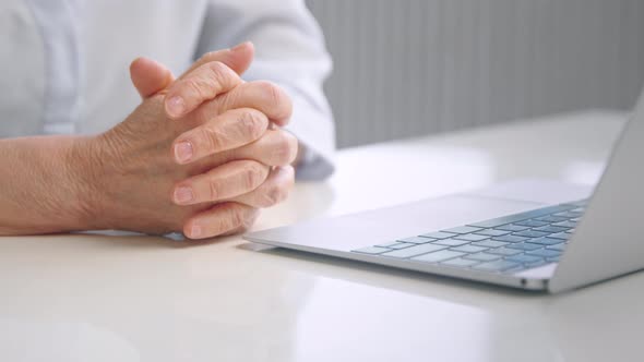 Worried old woman joins trembling wrinkly hands on white office