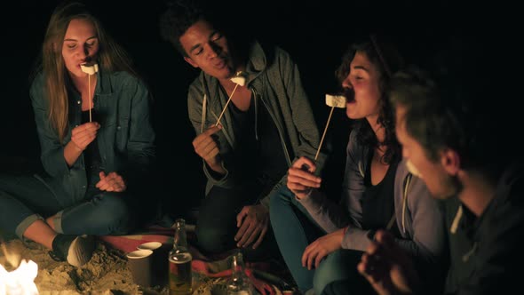 Group of Happy Multiethnic Friends Camping By the Fire at Night Laughing and Roasting Marshmallows