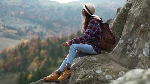 Woman Hiker in Hat Sits on Edge of Cliff and Looks Into Distance Mountain View Travel and Sports