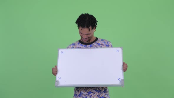 Happy Young Handsome African Man Holding White Board and Looking Surprised