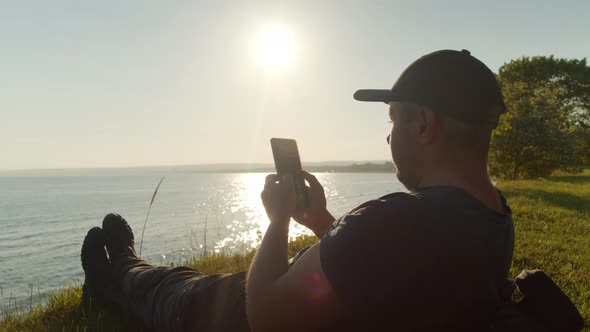 Male Traveler Uses Smartphone in Nature While Sitting Seashore