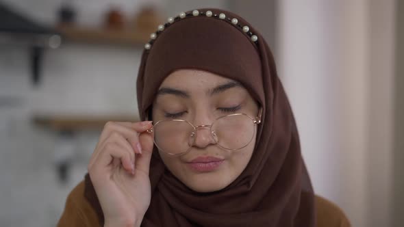 Headshot of Exhausted Middle Eastern Beautiful Woman in Hijab Putting Down Eyeglasses Looking at