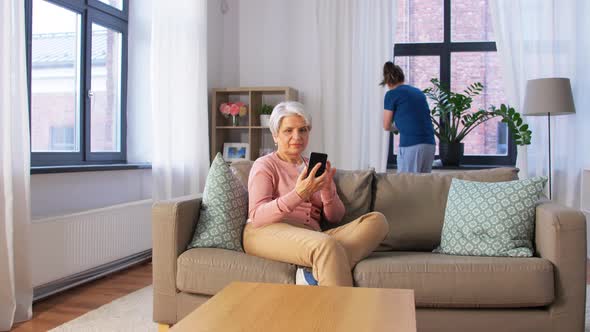 Old Woman with Smartphone and Housekeeper at Home