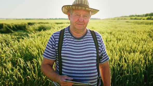 Successful Elderly Farmer Staying in Wheat Field with Digital Tablet and Happy Looking Into Camera