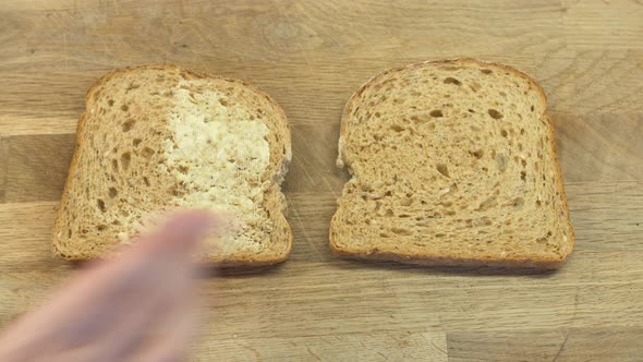 Wholemeal bread being buttered on a chopping board