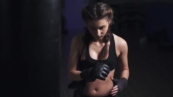 Woman Taking on Boxing Gloves on Hands with Black Boxing Wraps in Dark Room