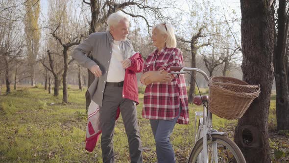 Handsome Senior Caucasian Gray-haired Man Putting Red Jacket on His Lovely Wife. Happy Mature