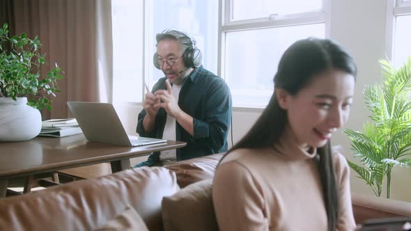 asian female wife hand use tablet on sofa with husband video conference at dining table