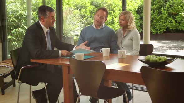 Wide shot off sales person showing documents to couple at dinning table