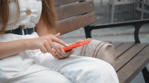 Woman Uses Smartphone Sitting On Bench in