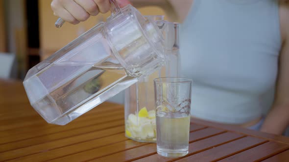 A Woman Pours a Tonic Drink with Lemon and Honey From a Decanter Into a Glass