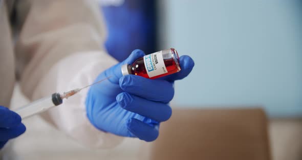 Doctor's Hand Holds a Syringe and a Red Vaccine Bottle at the Hospital