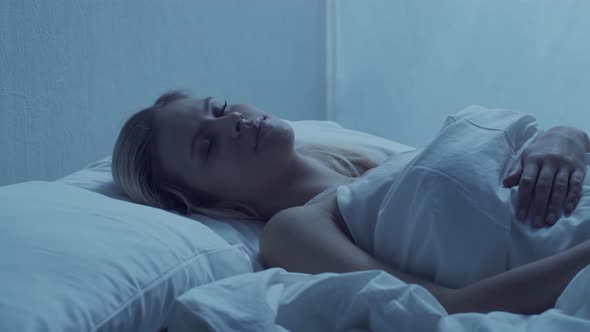Young woman lying in the bed at night. Beautiful sleeping girl. Twilight in the bedroom.