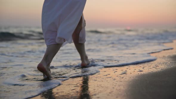 Young tourist with bare feet walking along the seashore at sunset