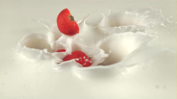 Super Slow Motion Halves of Strawberries Fall with Splashes in Milk