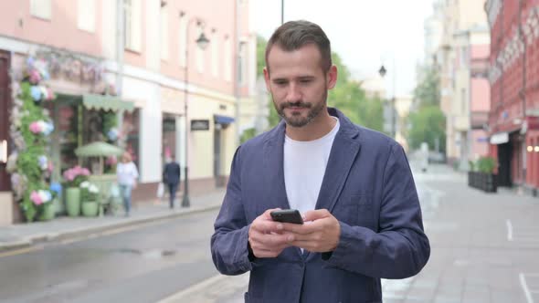 Man Using Phone While Walking on Beautiful Street