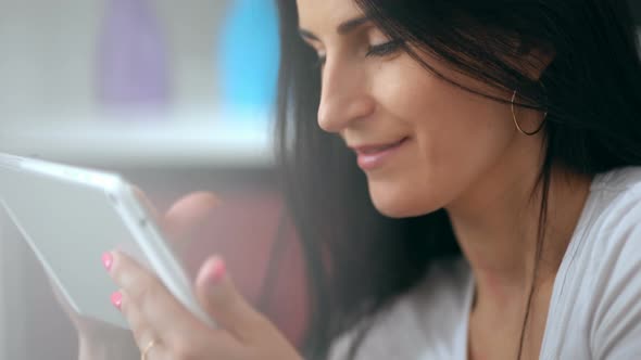 Beautiful Happy Young Woman Smiling and Using a Tablet at Home on Her Sofa