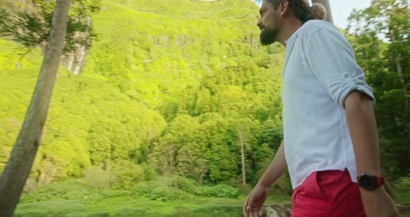 Man with a Beard and Ponytail Walks Towards the Pond Surrounded By Greenery