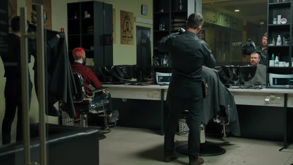 Two Hairdresser Masters Work with Clients in a Modern Barbershop