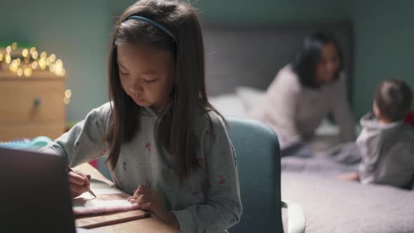 Meditative Asian girl painting while her family playing on the bed