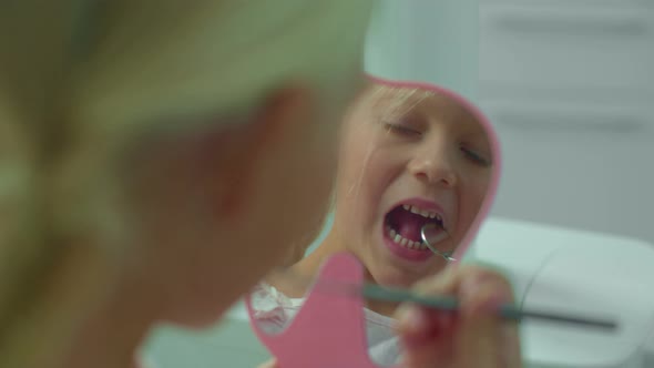 Little Girl Is Looking at Her Teeth in the Mirror.