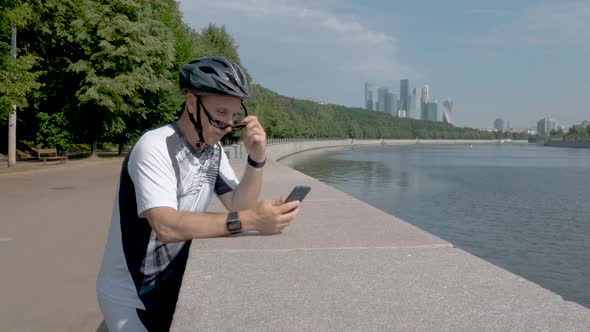 Cyclist in a Helmet and Sports Glasses, Watching an Application on His Smartphone.