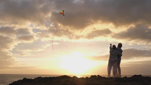 silhouette of a couple of people and mature seniors outdoors playing with a kite at the beach enjoy