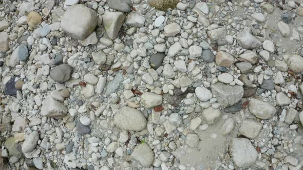 Flying over a riverbank full of rocks, pebbles and boulders in different colors