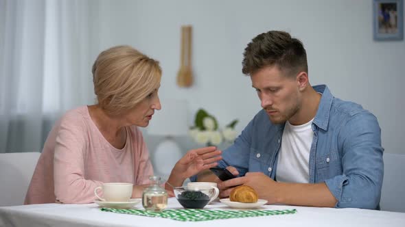 Worried Mother Talking to Infantile Adult Son Playing Video Games on Smartphone