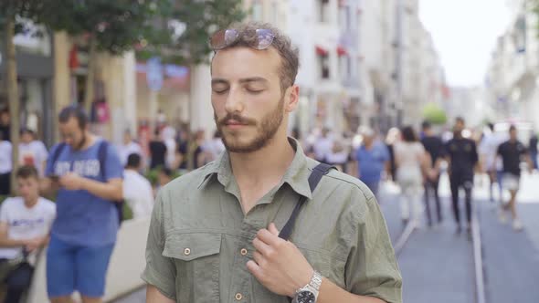 Young man with eyes closed in crowded street.