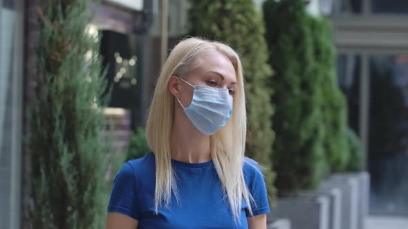 Portrait of a Charming Young Woman Looking at the Camera Putting on a Protective Medical Mask and