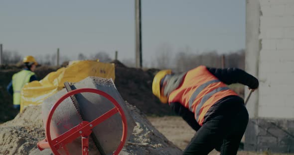 Male Worker Putting Cement in Mixer with Shovel