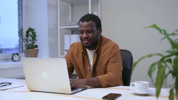 African Happy Man at Computer Works in Room with Plant Spbas