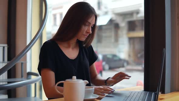 Young Woman Sitting in the Coffee Shop Having a Coffee Break She is Opening Her Laptop and Starts