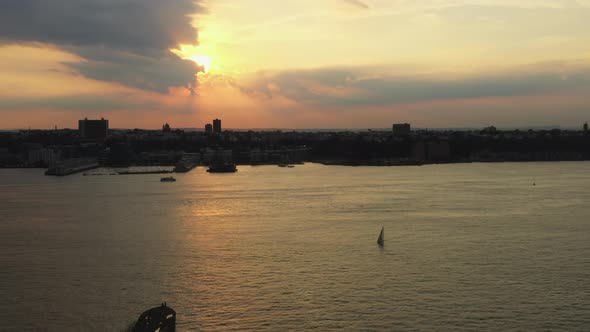 drone ascends, truck right up to golden sunset with ferry & sailboat on the Hudson River with New Je