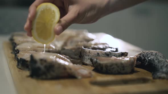 Female Hands Pouring Fish Fillet with Lemon Juice on Wooden Tablet