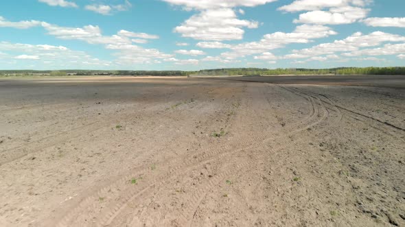 Flying Over a Row of Cultivated Soil Behind a Tractor Visible in the Distance