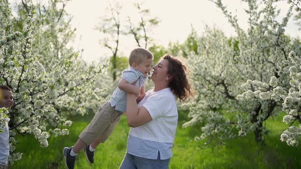 Mom Plays in the Spring Garden with a Young Son Swirls and Throws the Child Up