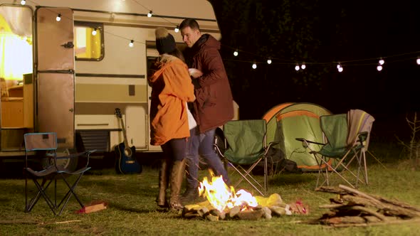 Cheerful Young Couple Dancing Around Camp Fire in Cold Night of Autumn