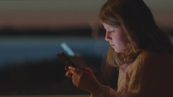 Young Girl Playing On Smartphone At Dusk