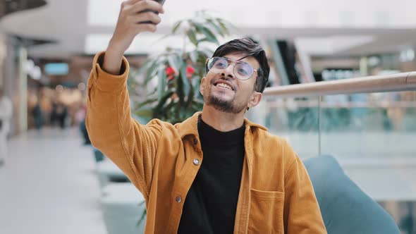 Young Happy Indian Guy Blogger Holds Smartphone Recording Vlog Filming Video for Blog in Mall Joyful