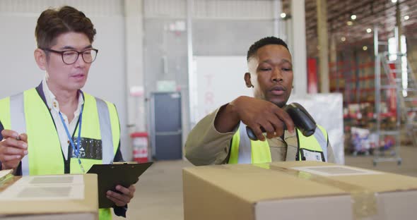 Diverse male workers wearing safety suits and scanning boxes in warehouse