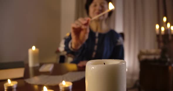 Big White Candle Standing at the Foreground As Blurred Old Caucasian Woman Lighting Up Candles