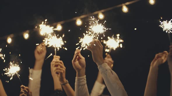 Closeup of Hands or Palms Holding and Waving Burning Sparklers in Front of Black or Dark Background